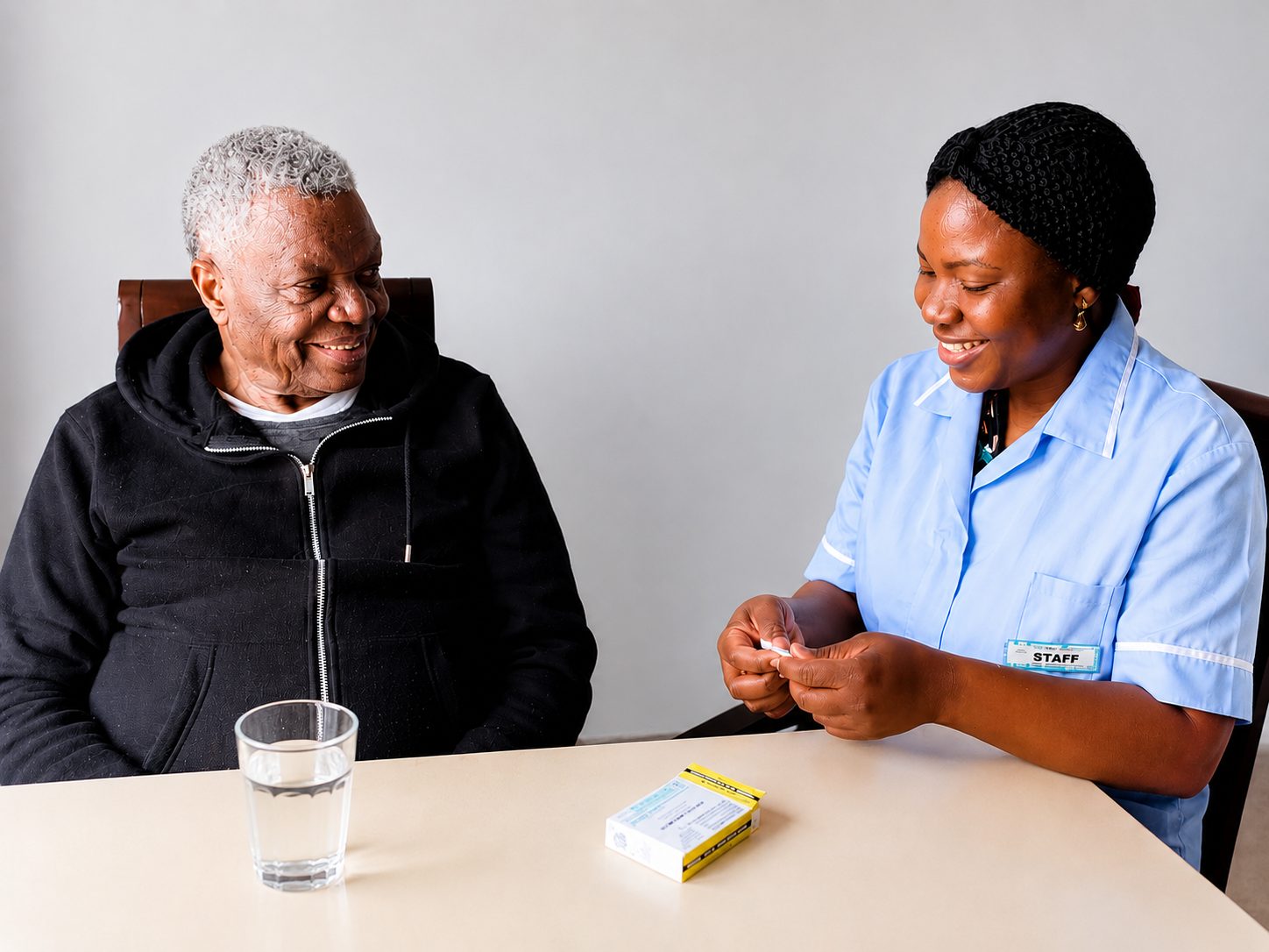 An Angeliquecare carer helping an elderly man with his medication at the table